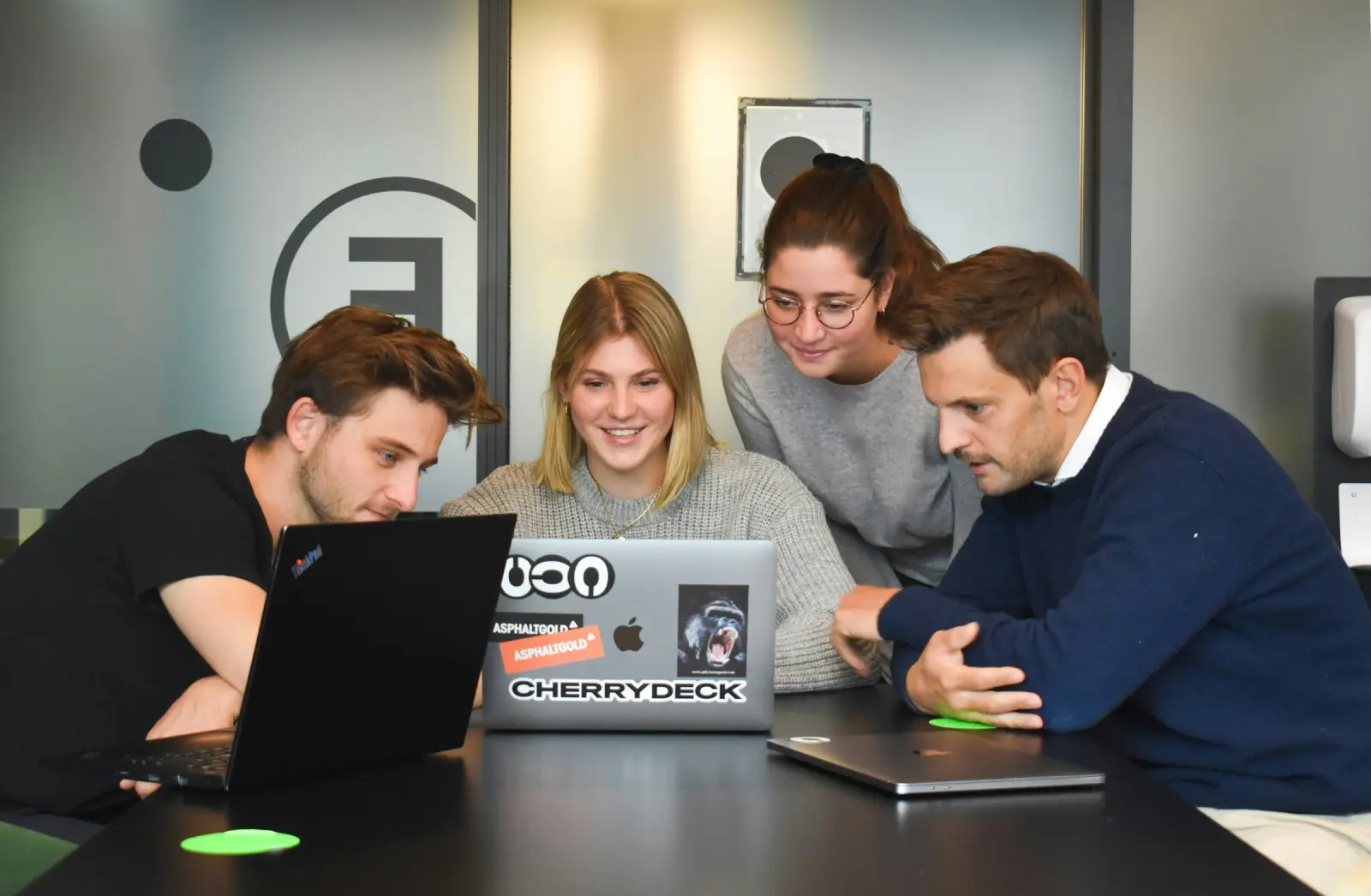 Four people collaborating around a laptop in a meeting room