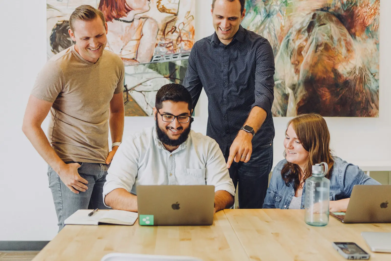 Four coworkers smiling around a laptop at a shared table