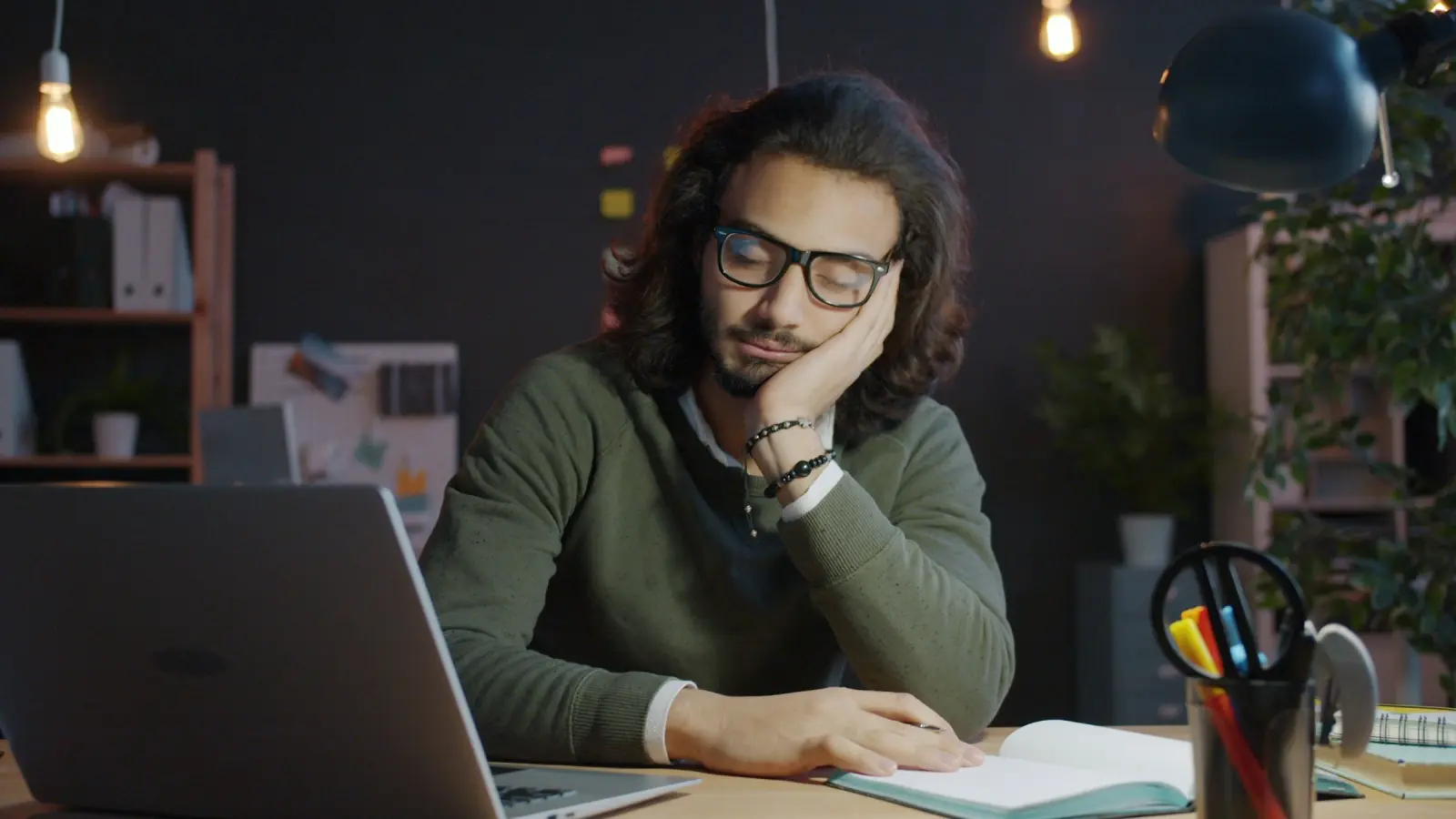 A man slumped at his desk beside a laptop and notebook